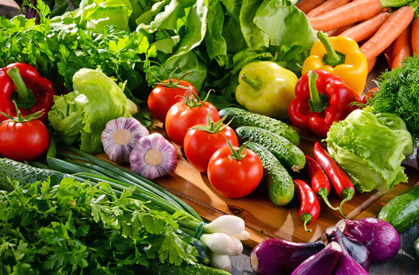 Assorted fresh organic vegetables including tomatoes, peppers, cucumbers, carrots, lettuce, and herbs without pesticides